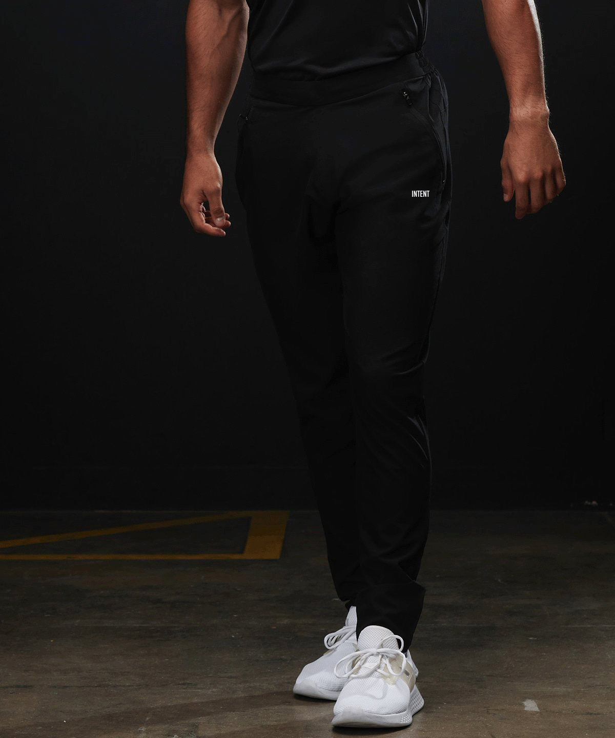 Person wearing black jogger pants with a brand logo on a dark background