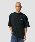 Person wearing a black oversized t-shirt and blue pants against a beige background