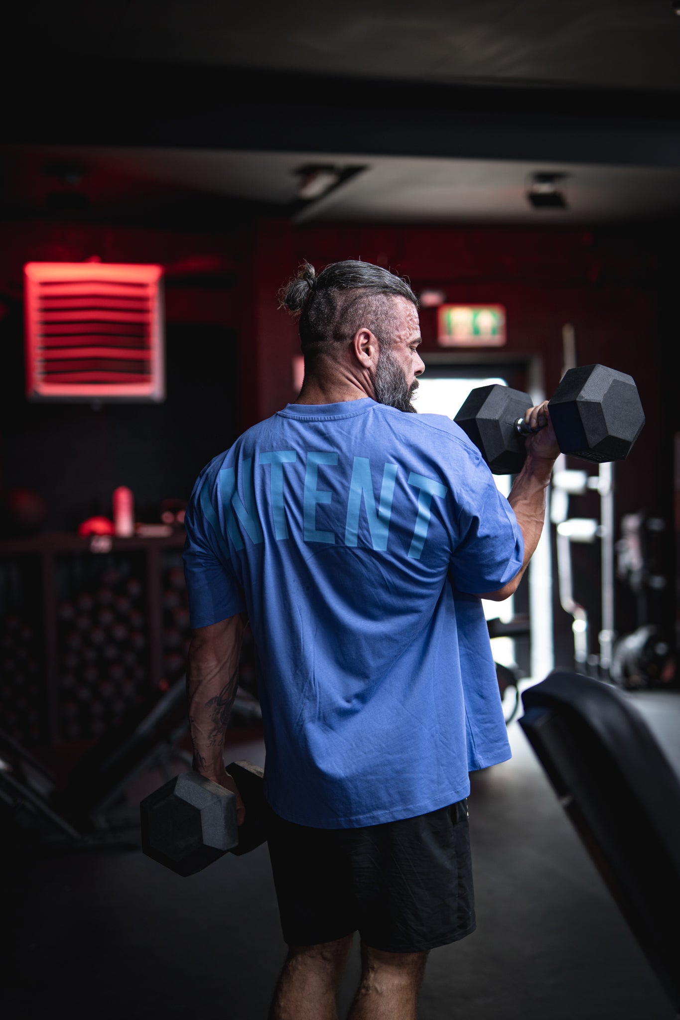 Man lifting dumbbells in a gym setting with red lighting