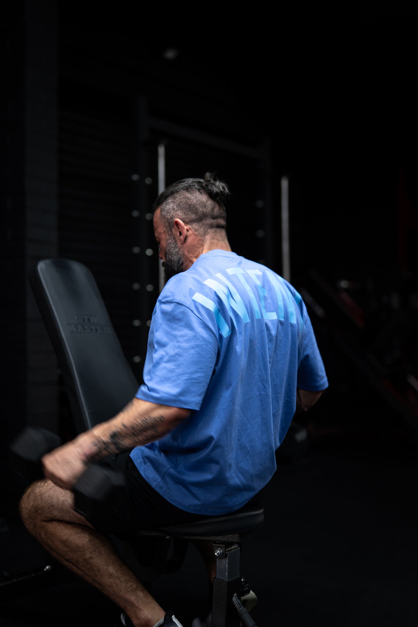 Man in a blue shirt sitting on a black exercise bike in a dark room