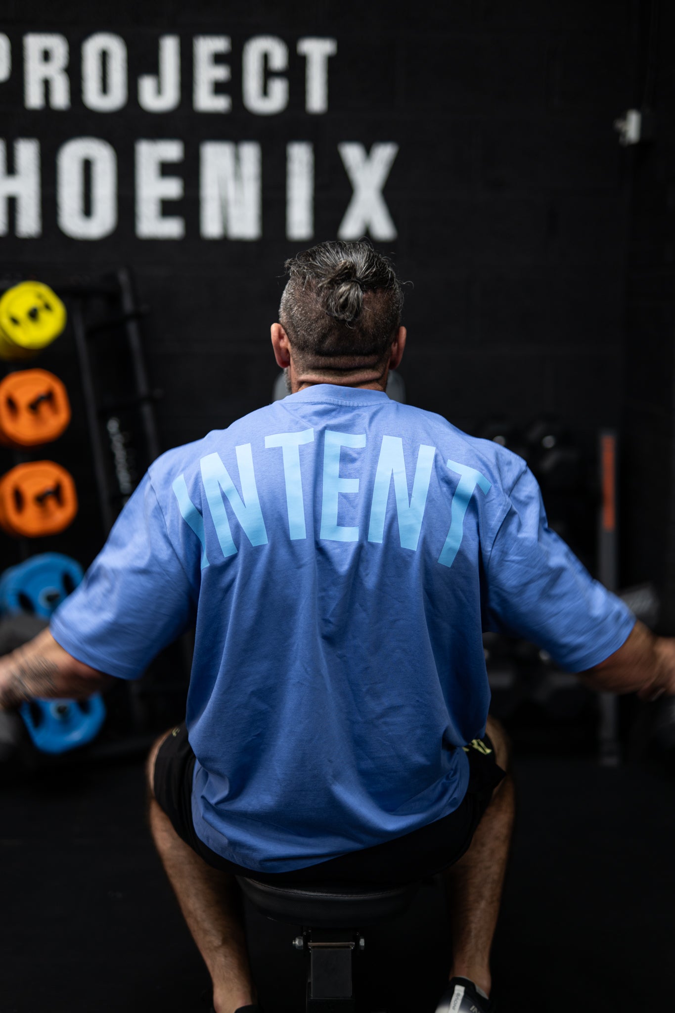 Person wearing a blue shirt with 'Intent' on the back, standing in front of a black wall with 'Project Phoenix' text.