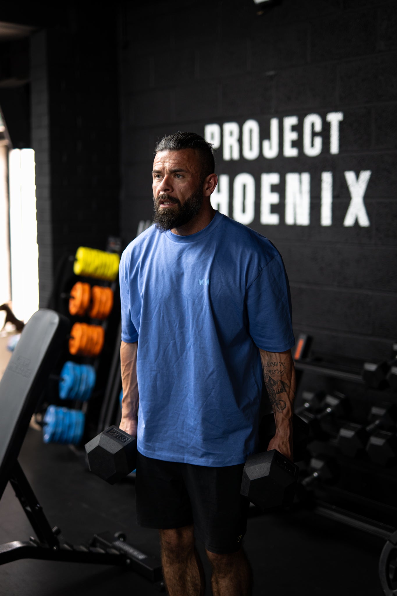 Man in a blue shirt standing in a gym with 'Project Phoenix' on the wall.