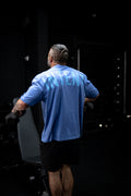 Man in a blue shirt and black shorts standing in front of a dark background
