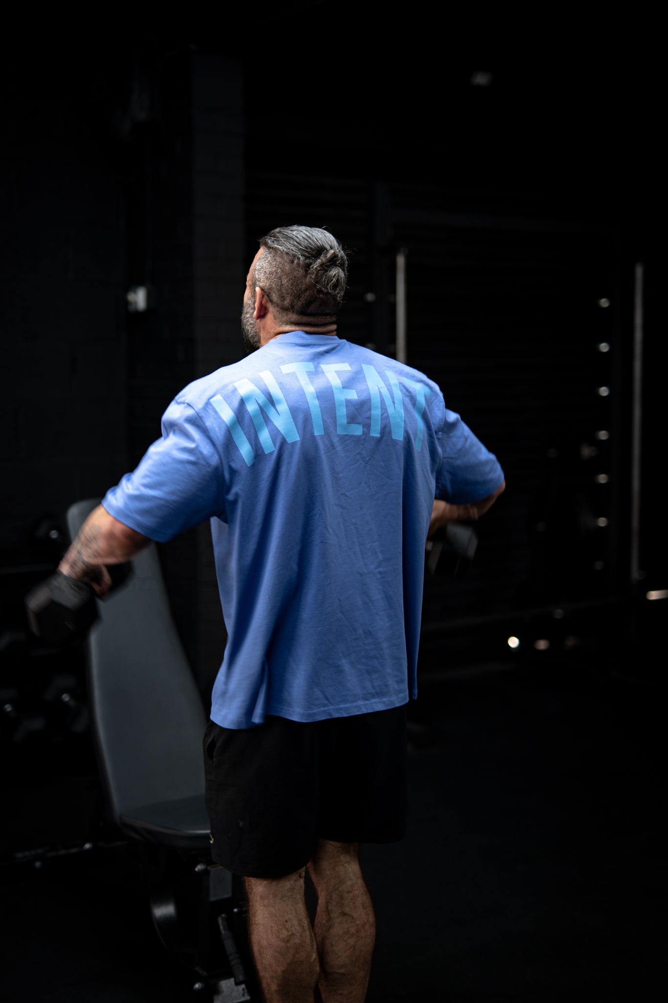 Man in a blue shirt and black shorts standing in front of a dark background