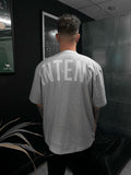 Person wearing a gray 'INTENT' t-shirt in a dark room.