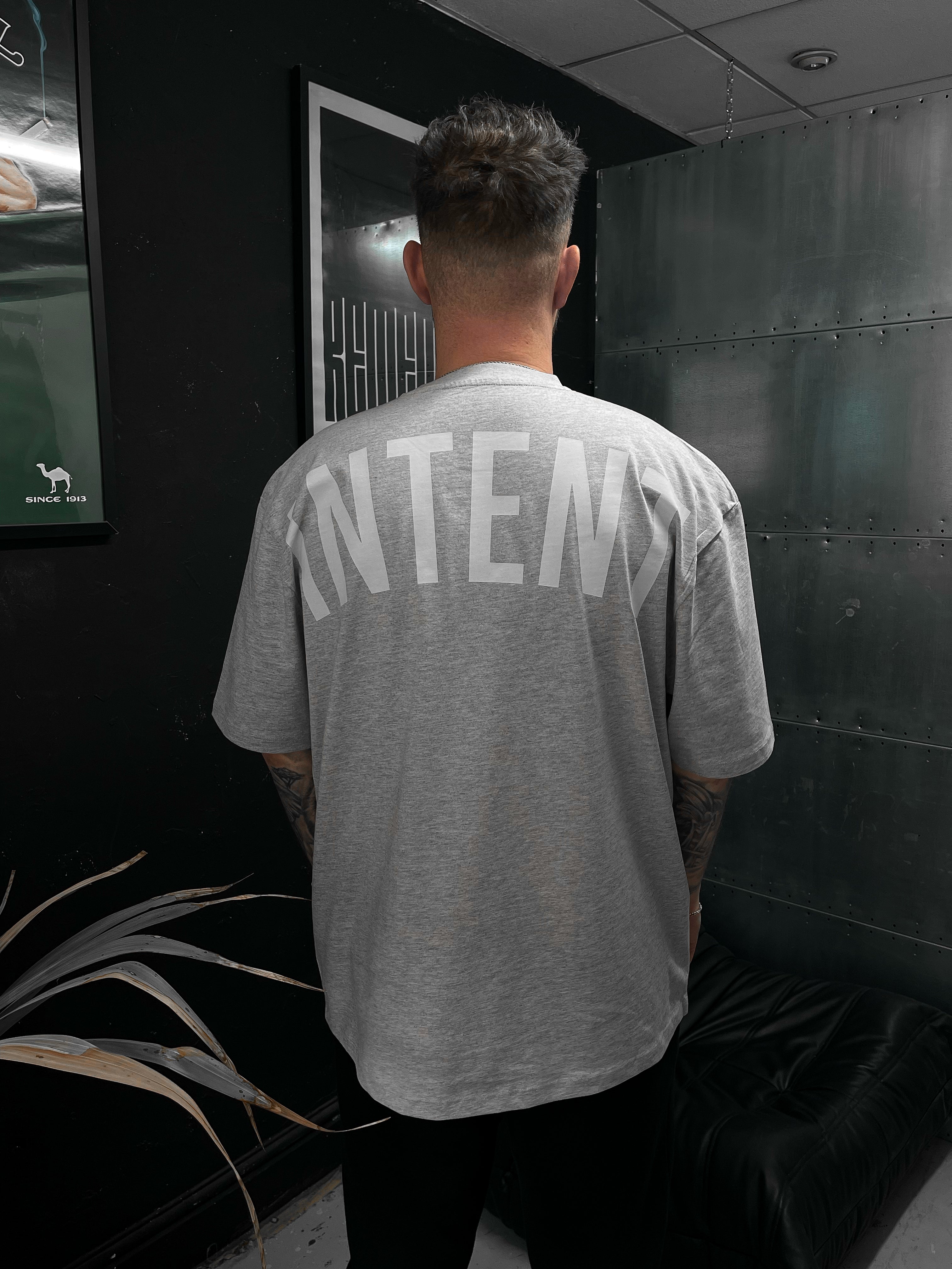 Person wearing a gray 'INTENT' t-shirt in a dark room.