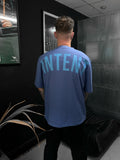 Person wearing a blue t-shirt with 'INTENT' printed on the back in a room with black walls and a plant.