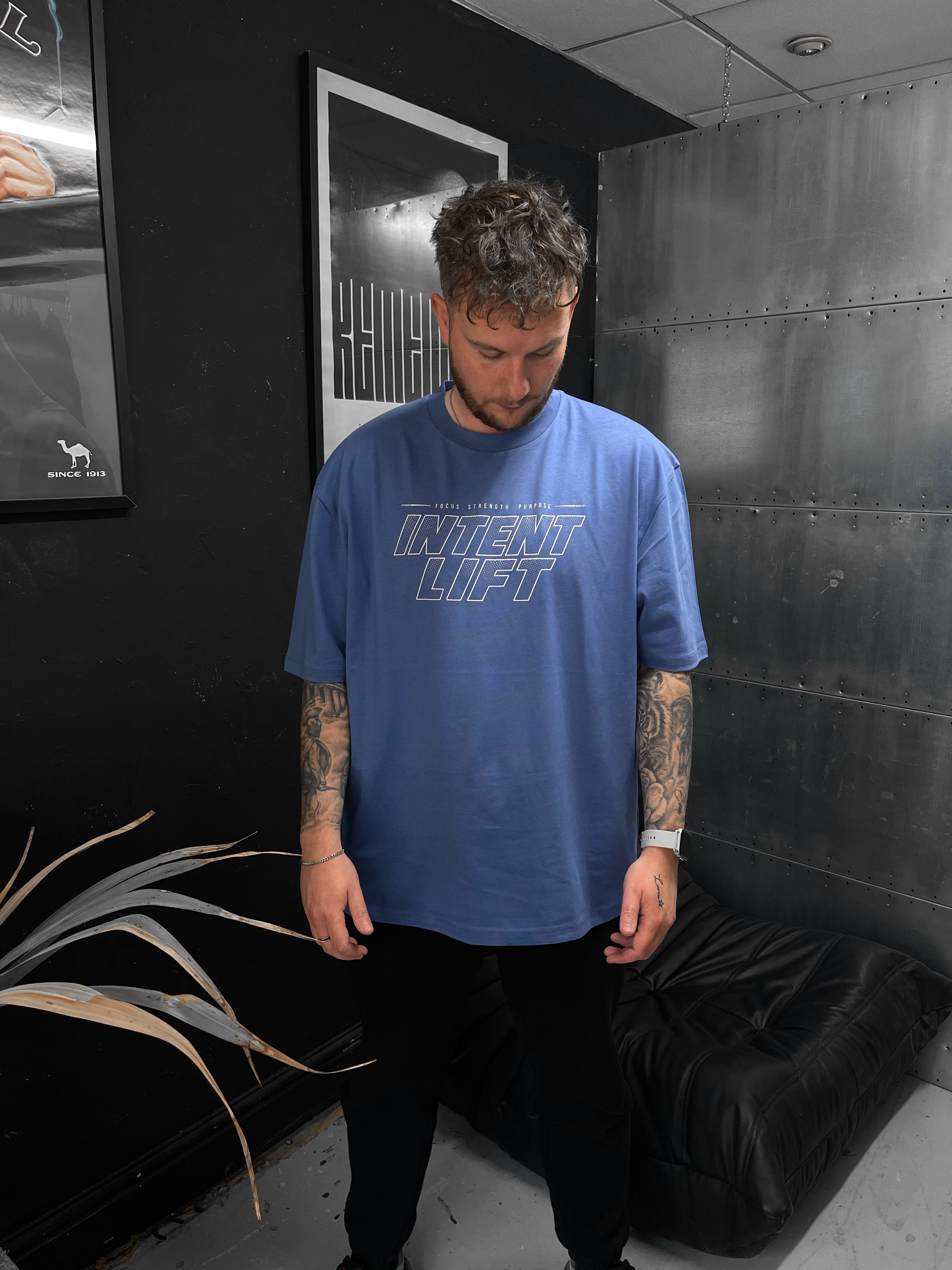Man wearing a blue t-shirt with 'Invent Lift' text in a room with black walls and a plant.