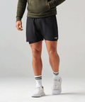 Person wearing black athletic shorts with a brand logo on a light gray background