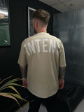 Person wearing a beige t-shirt with 'INTENT' printed on the back in a dark indoor setting.